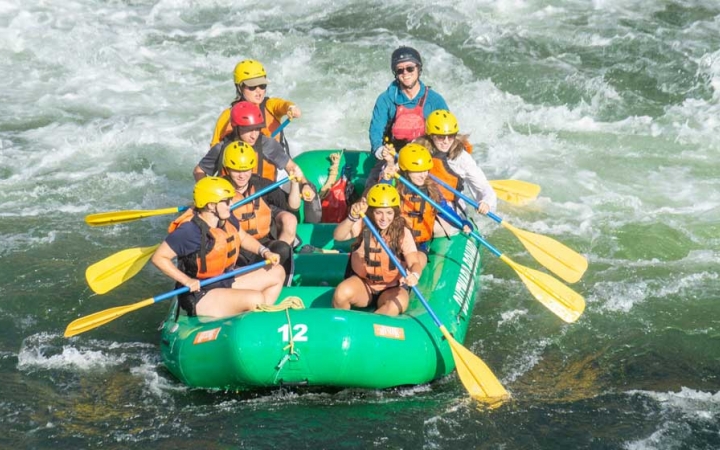 a group of outward bound students wearing helmets and life jackets paddle a raft through whitewater